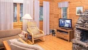 Interior acolhedor de uma cabana, com decoração em madeira, lareira de pedra, televisão e área de estar confortável.
