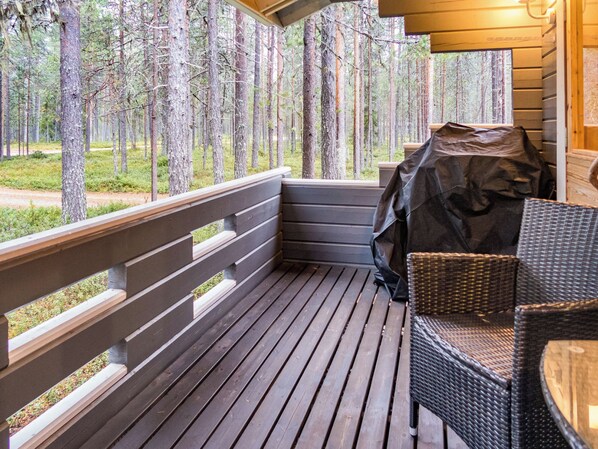 A wooden deck with a railing, a wicker chair, and a grill.