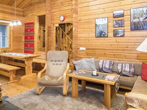 A cozy cabin interior with a wooden interior, a sofa, a chair, a table, and a fireplace.