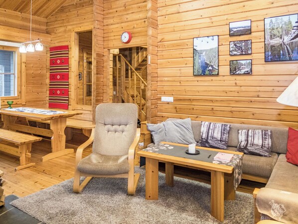 A cozy cabin interior with a wooden interior, a sofa, a chair, a table, and a fireplace.