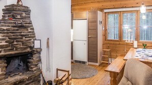 Interior acolhedor de uma cabana com lareira de pedra, área de jantar e vista para a floresta através de grandes janelas.