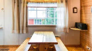A wooden picnic table with a window above it, curtains, a small shelf with a radio, and a wooden floor. - Soidinaukea b 20 by Interhome (Inari)