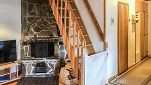 A cozy living area with a stone fireplace, wooden staircase, and a television on a stand. - Soidinaukea b 20 by Interhome (Inari)