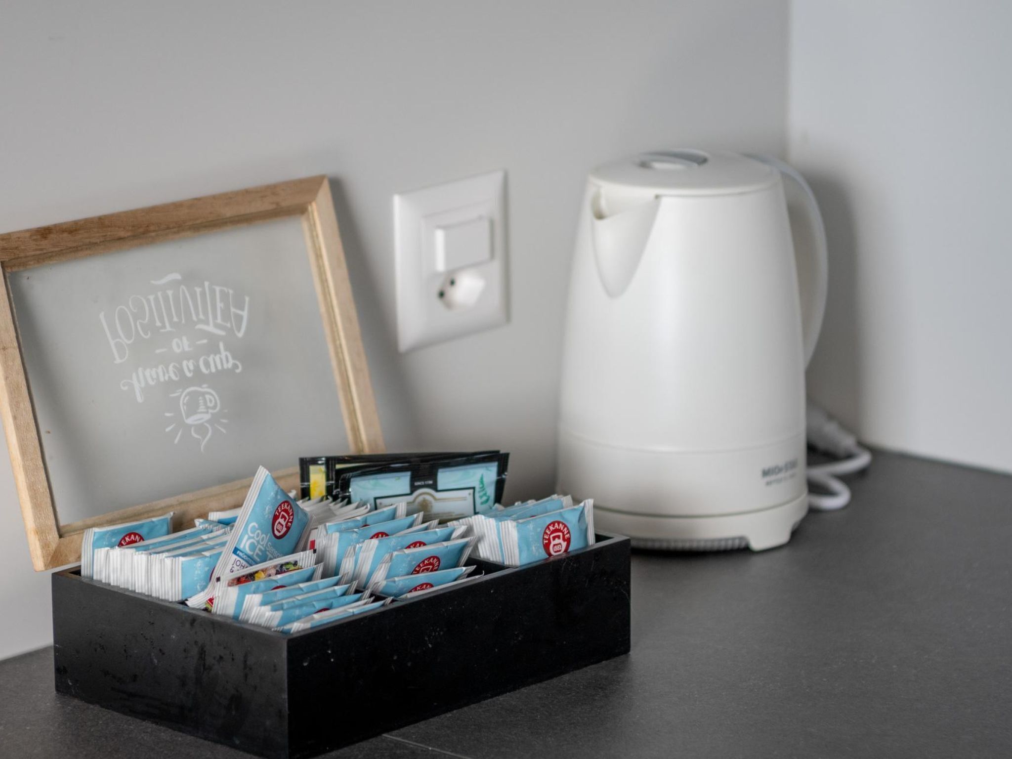 A black box with coffee packets and a framed sign on a table next to a white coffee maker.
