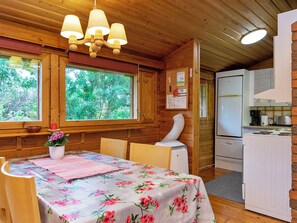 Interior de una cabaña de madera con una mesa de comedor, sillas, un refrigerador y una zona de cocina.