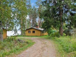 A cabin with a gravel path leading to it, surrounded by trees and a body of water.