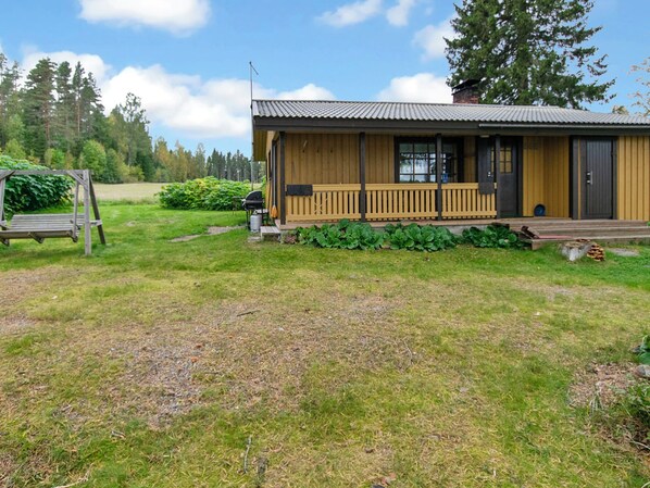 A wooden cabin with a porch, surrounded by a grassy yard and trees.