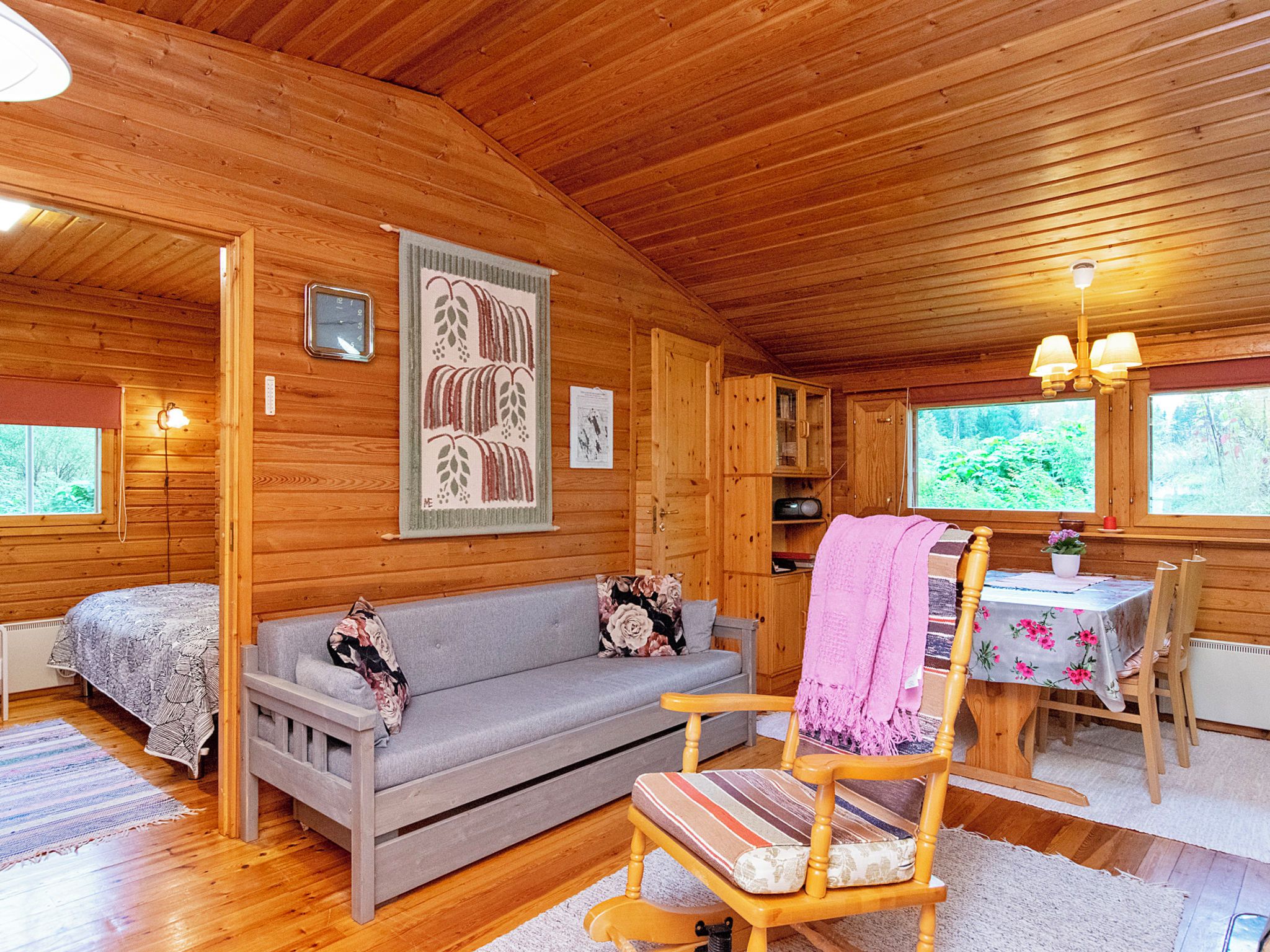 Ein gemütliches Blockhaus-Interieur mit einer Couch, einem Sessel, einem Esstisch und einem Fenster mit Blick auf Grünfläche.