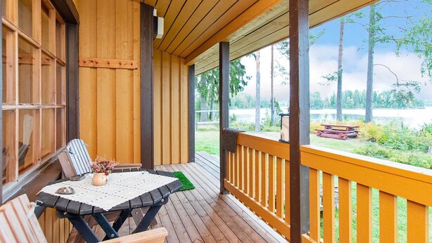 Una terrazza in legno coperta con tavolo e sedie, affacciata su un paesaggio naturale.