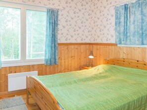 Un dormitorio con cabecera de madera, colcha verde, lámpara de noche y ventana con cortinas.