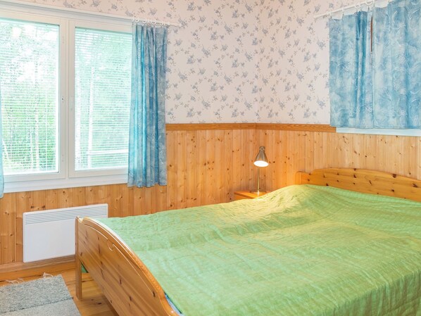 A bedroom with a wooden headboard, a green bedspread, a bedside lamp, and a window with curtains.