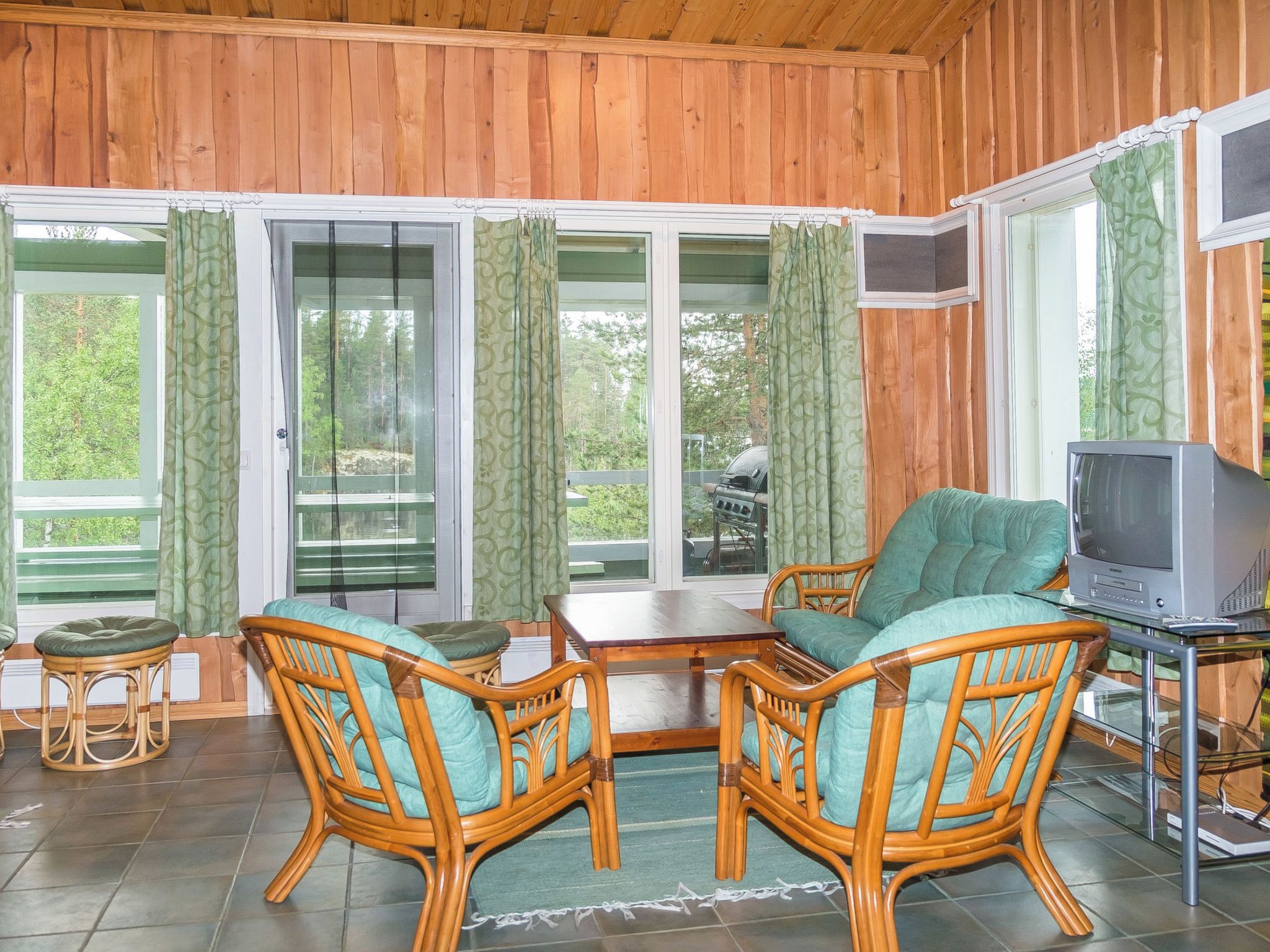 A wooden-paneled room with wicker furniture, a television, and large windows with curtains.
