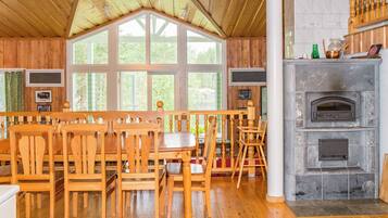 Un interior de madera con chimenea, ventanas amplias y una zona de comedor con mobiliario de madera.