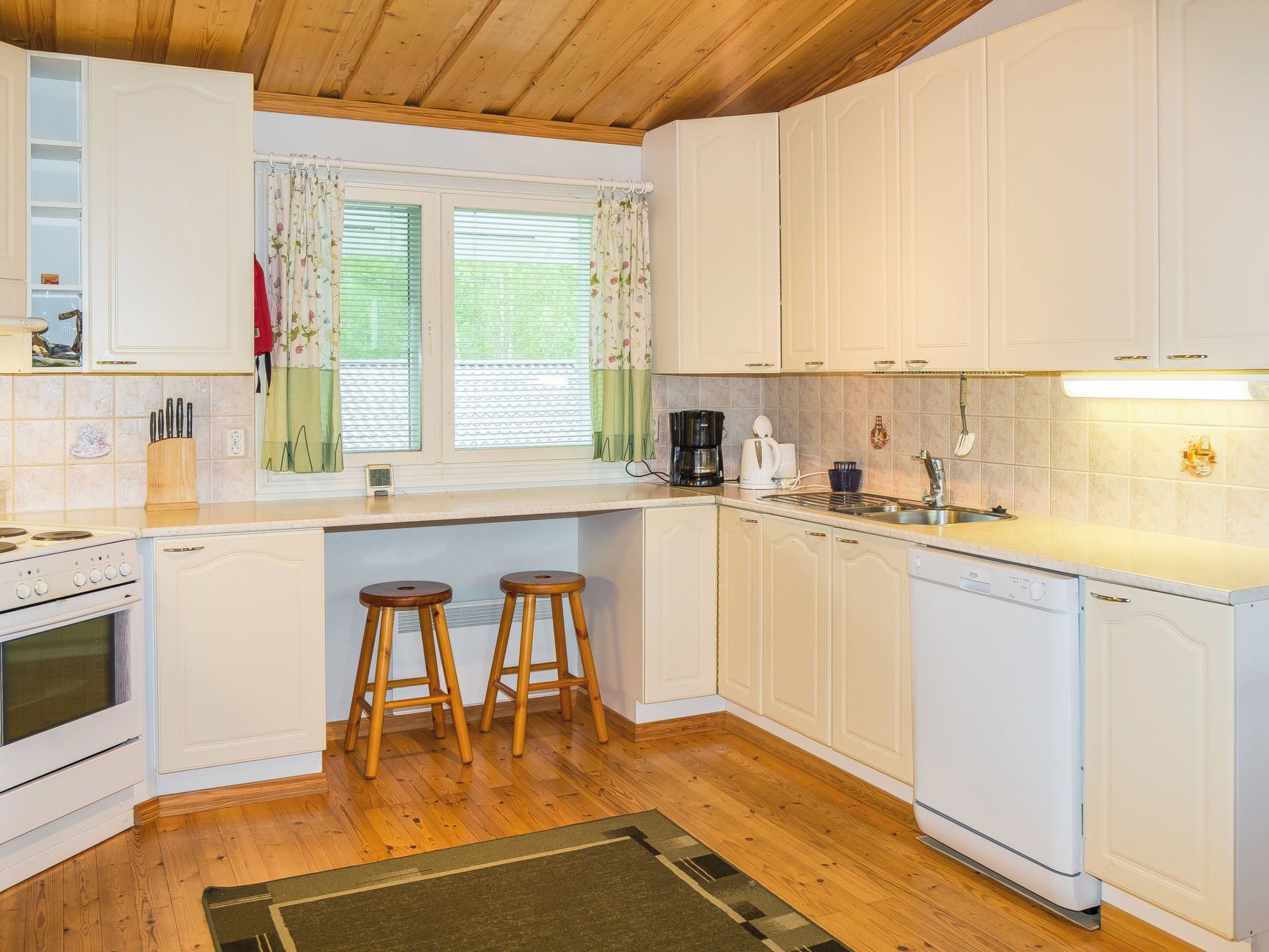 A kitchen with white cabinets, a stove, a coffee maker, and two stools.