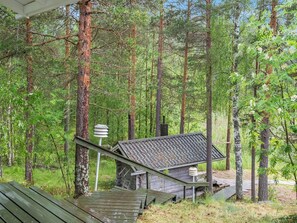 A wooden cabin with a sloped roof, surrounded by a forest.