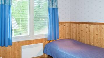 Quarto com cama, paredes de madeira, janela com cortinas e radiador.