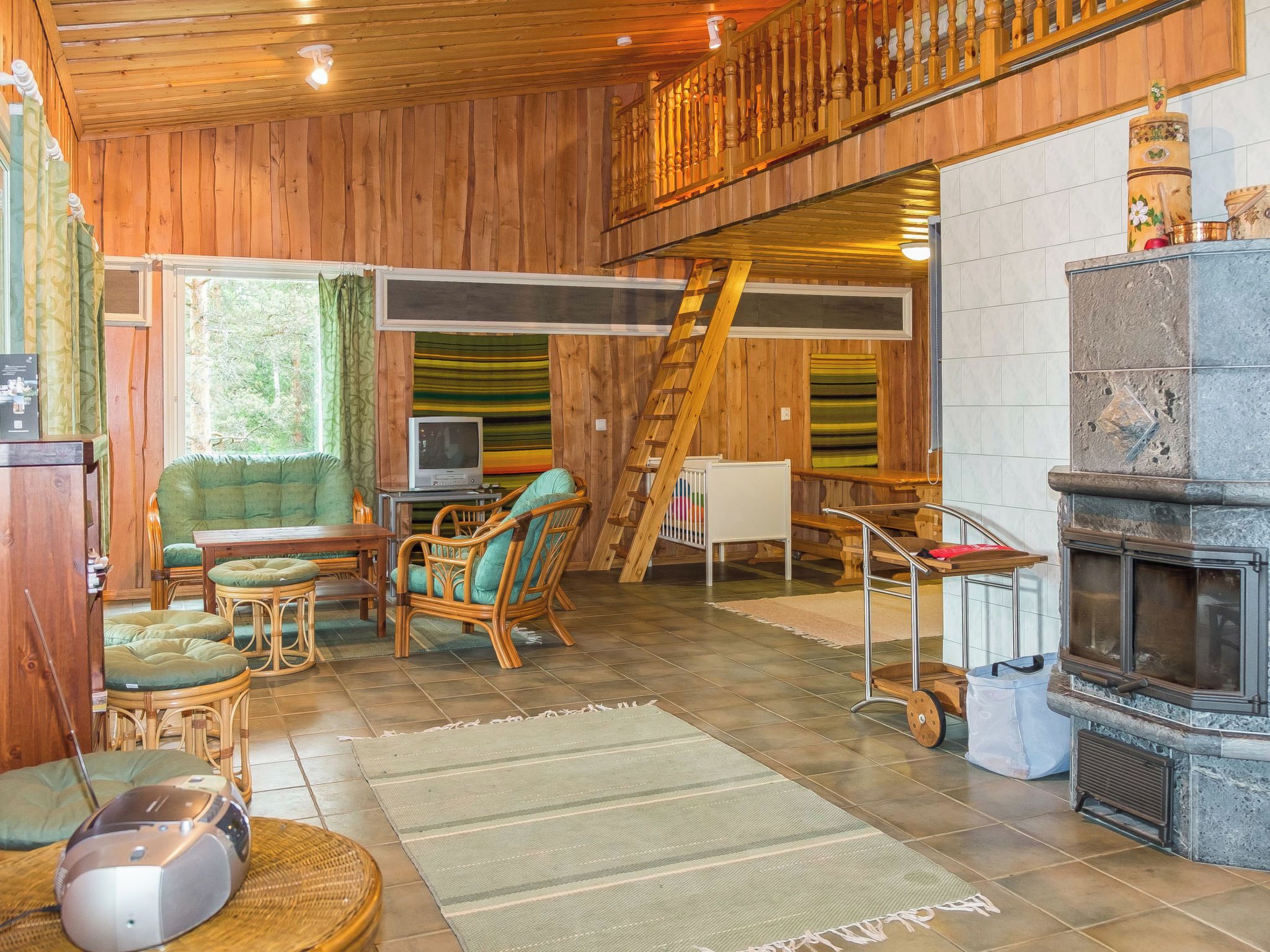 A cozy cabin interior with a fireplace, wooden walls, a dining area with chairs, a television, and a ladder.
