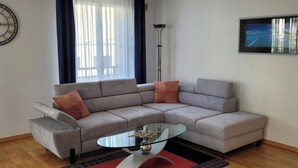 Ein modernes Wohnzimmer mit einem grauen Ecksofa, einem Glastisch und einem Teppich in Rot und Schwarz.