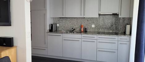 A modern kitchen with grey cabinets, a granite countertop, and a built-in oven.