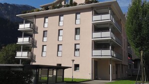Ein mehrgeschossiges Gebäude mit Balkonen, einer flachen Dachterrasse und einem Berg im Hintergrund.