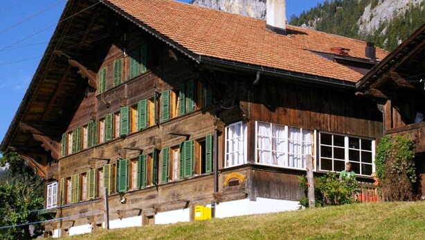 En traditionel træchalet med skråtag, store vinduer og skorsten.