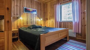 A wooden-paneled room with a bed, two bedside lamps, a window with curtains, and a wall-mounted picture.
