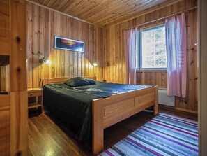 Een kamer met houten lambrisering, een bed, twee bedlampen, een raam met gordijnen en een aan de muur hangend schilderij.