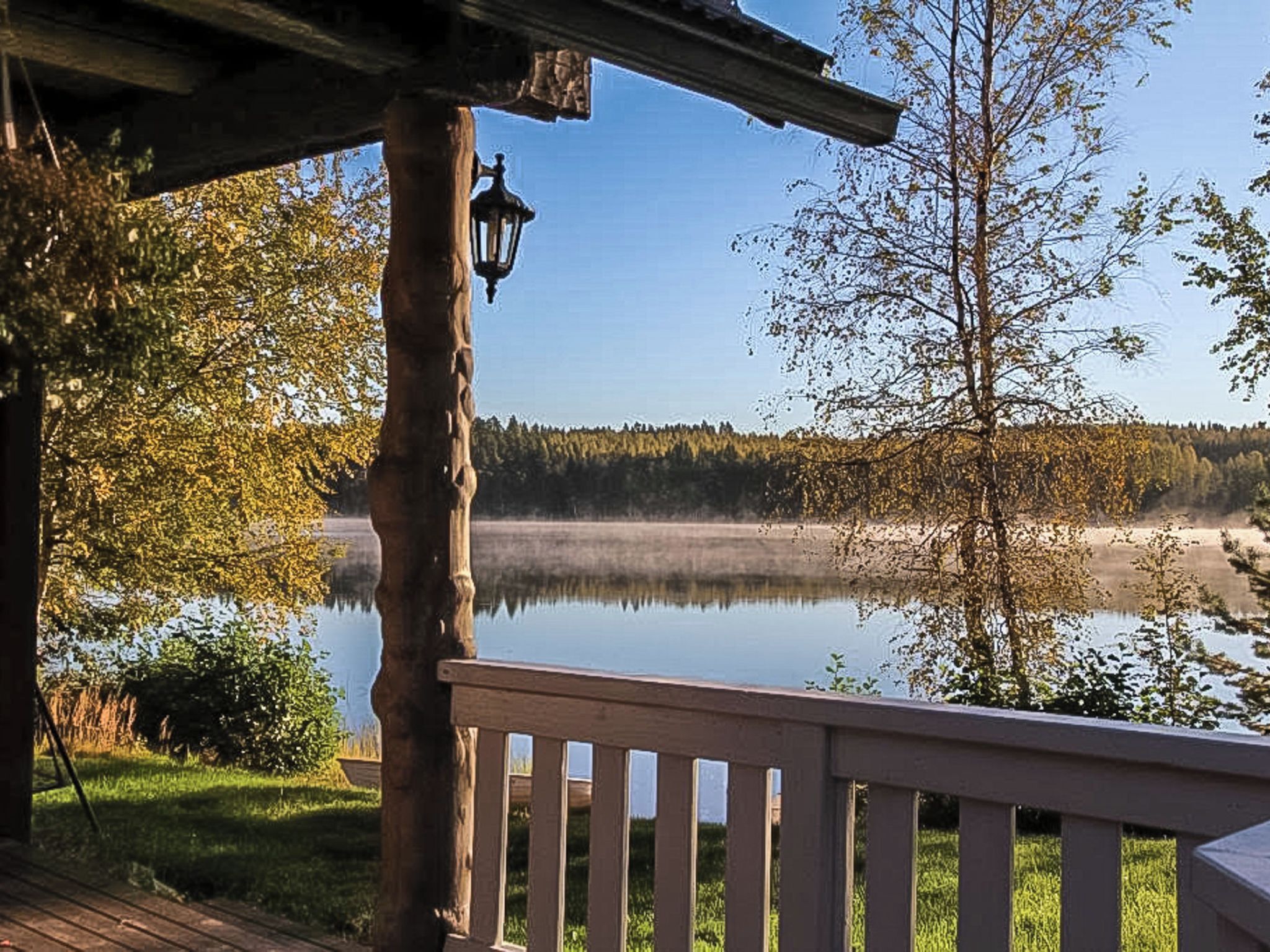 Une terrasse en bois avec une rambarde donnant sur un lac paisible et une forêt.