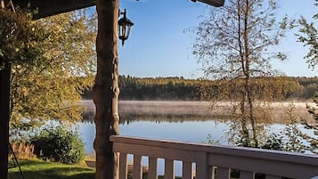 Une terrasse en bois avec une rambarde donnant sur un lac paisible et une forêt.