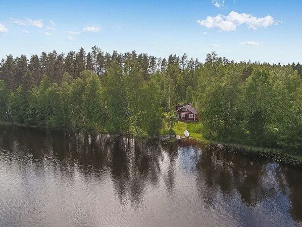 A lakeside cabin with a dock, surrounded by dense forest and calm water.
