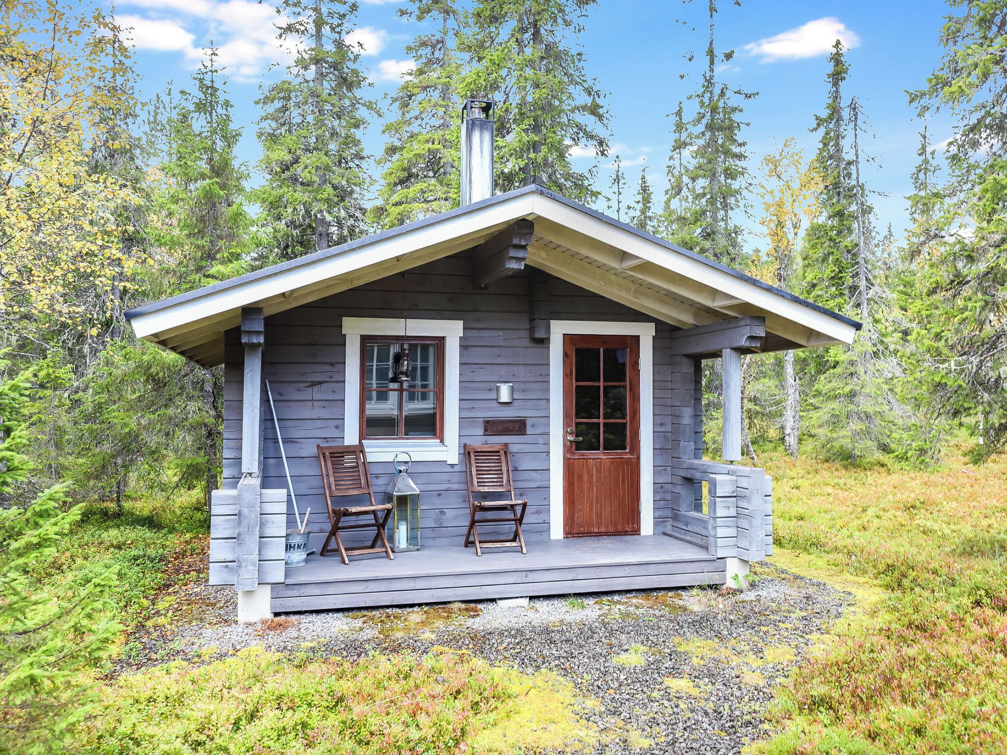 A cabin with a porch, two wooden chairs, a small table, and a window.