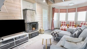 A cozy living room with a stone fireplace, a flat-screen TV, a grey sofa, and plaid chairs.