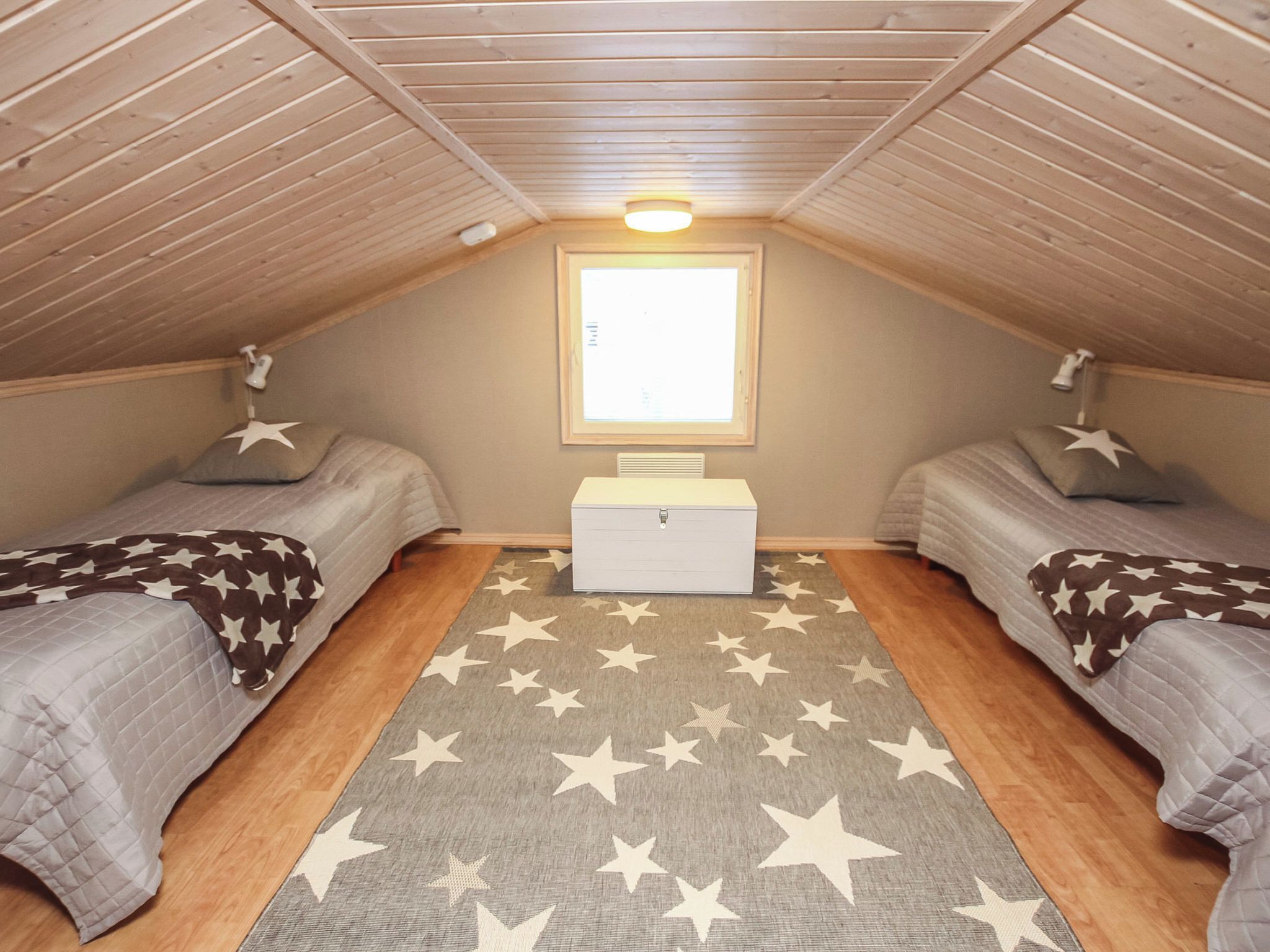A small, cozy attic bedroom with two beds, a window, and a star-patterned rug.