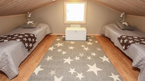A small, cozy attic bedroom with two beds, a star-patterned rug, and a window providing natural light.
