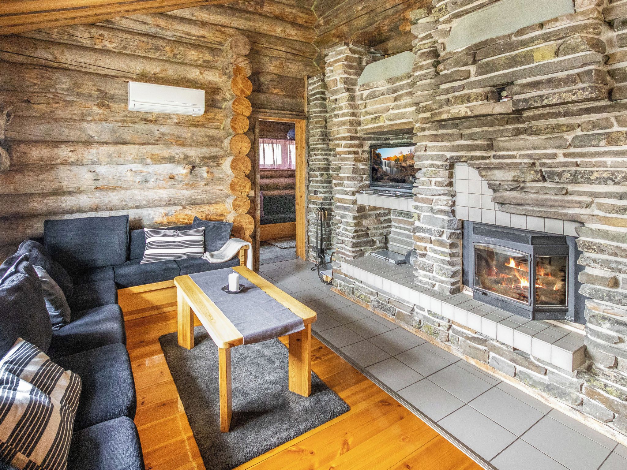 A log cabin interior with a stone fireplace, a sofa, and a wooden table.