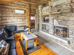 A log cabin interior with a stone fireplace, a sofa, and a wooden table.
