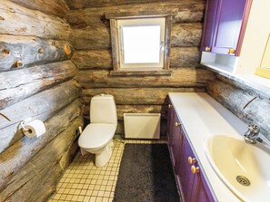 Een badkamer in een blokhut, met een toilet, een raam, een radiator en een bad.