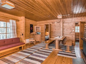 L'intérieur d'une cabane en rondins, avec un canapé, une table à manger, une chaise, un lit et une cheminée.