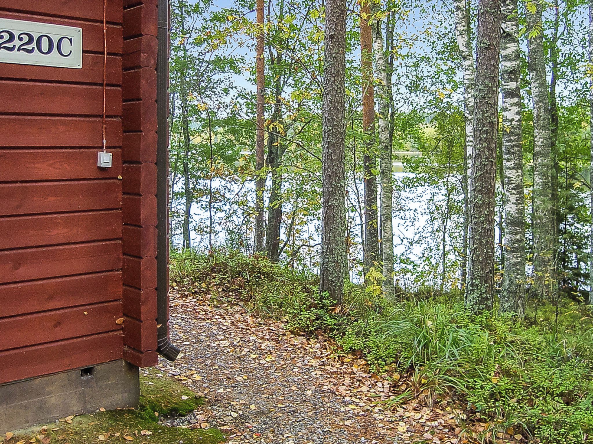 A wooden cabin with a sign reading '220C' adjacent to a forested area with a body of water.