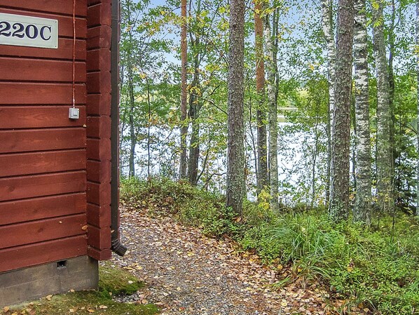 A wooden cabin with a sign reading '220C' adjacent to a forested area with a body of water.