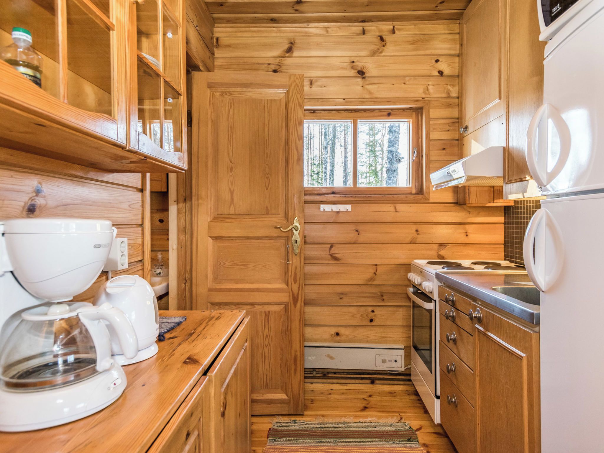 Cocina compacta con muebles de madera, cafetera, microondas y ventana con vistas a árboles.