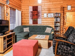 Interior acogedor de una cabaña de troncos con un sofá modular, un televisor, una estantería y un tapiz grande.