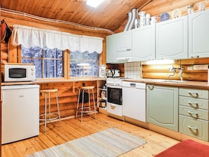 A compact kitchen with wooden walls, a window with a view of a snowy landscape, a microwave, a coffee maker, and a dishwasher.