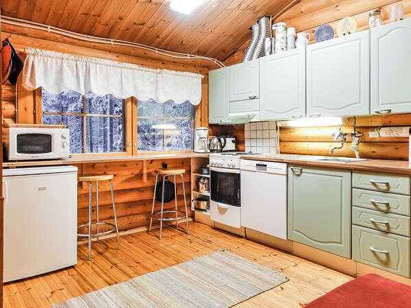 Cocina pequeña con paredes de madera, ventana con vistas a un paisaje nevado, microondas, cafetera y lavavajillas.
