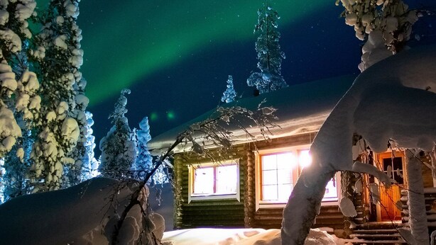 A log cabin with a window, surrounded by snow-covered trees and a snowy landscape.