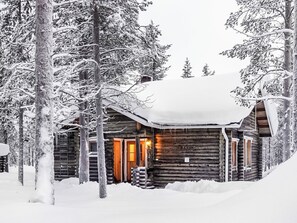 A log cabin with a snow-covered roof, surrounded by trees.