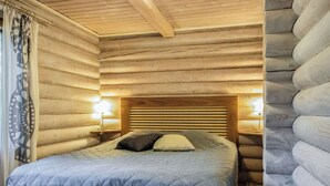 A log cabin bedroom with a bed, two bedside lamps, and a window with curtains. - Kalliohonka by Interhome (Hämeenlinna)