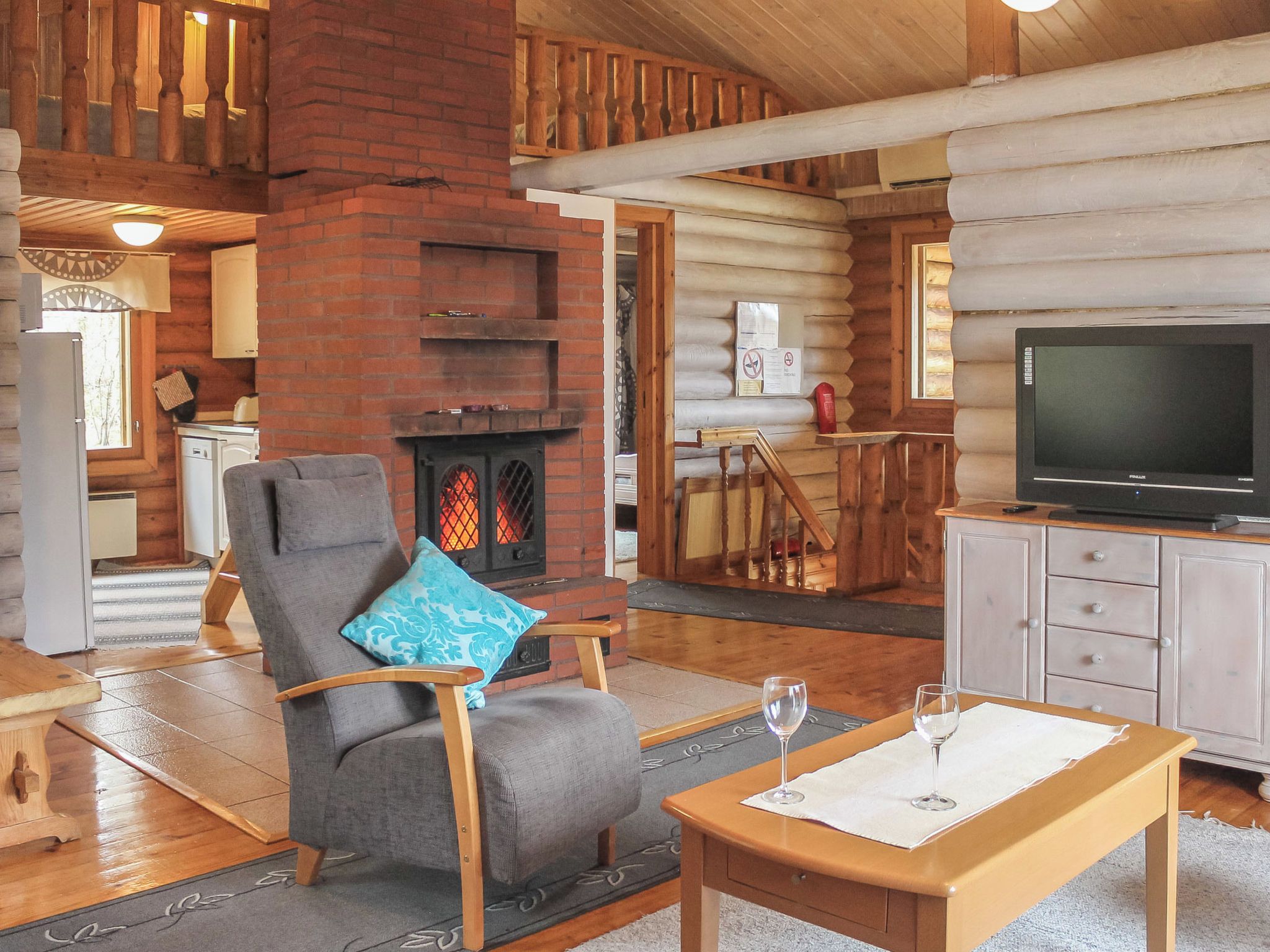 A log cabin interior with a fireplace, a television, a dining area, and a seating area.