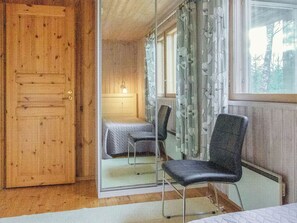 Ein Zimmer mit Holztür, einem Bett mit weißer Bettdecke, einem Stuhl und einem Fenster mit Vorhängen.
