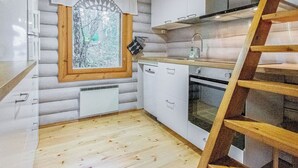 A compact kitchen with wooden cabinets, a built-in oven, and a window with a view of trees. - Kalliohonka by Interhome (Hämeenlinna)